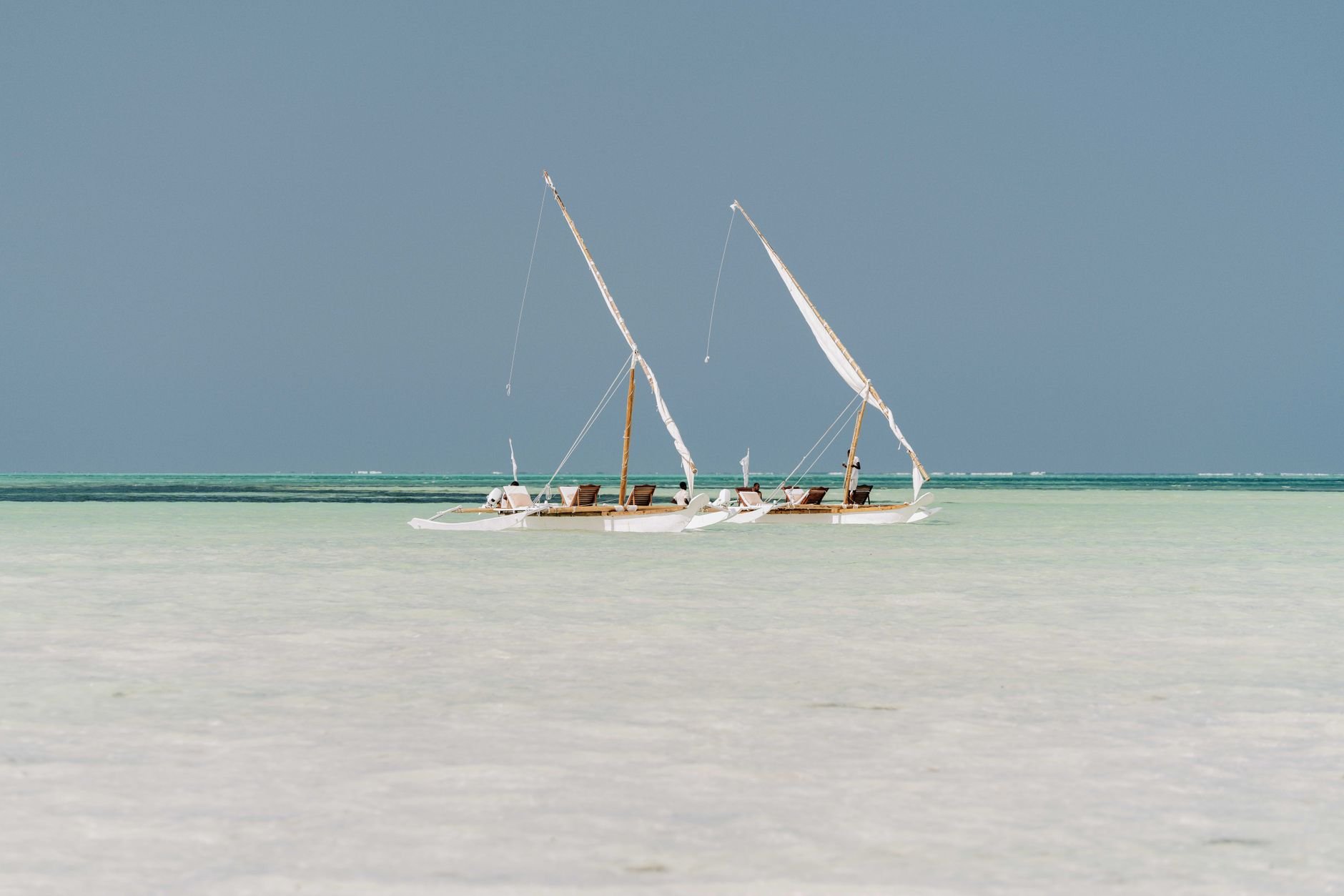 Serene scene of traditional dhows sailing on Zanzibar's turquoise waters under a clear sky.